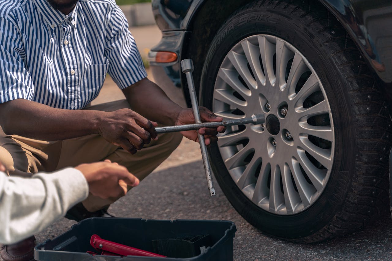 An adult demonstrating how to change a tire to a teenager, focusing on teamwork and learning.